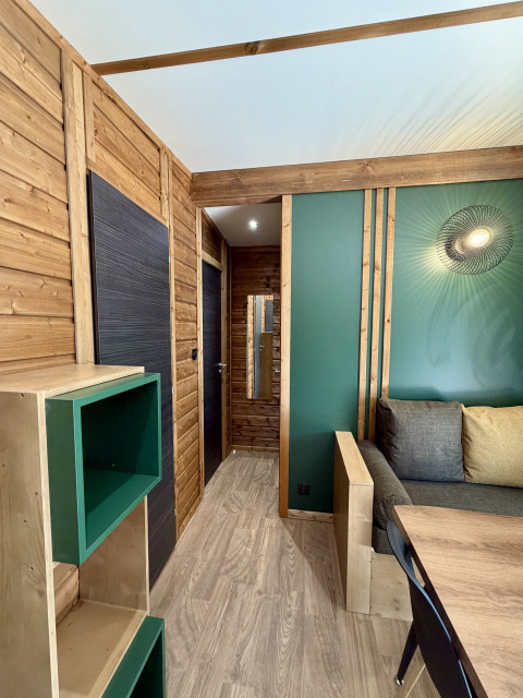 Interior of a modern lodge at La Clairiere, Campsite Seasonova Ensoya, France, featuring wood panel walls and green accents.
