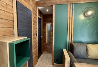 Interiør af en moderne hytte i La Clairiere ved Campsite Seasonova Ensoya, med trævægge, grønne detaljer og møbler.