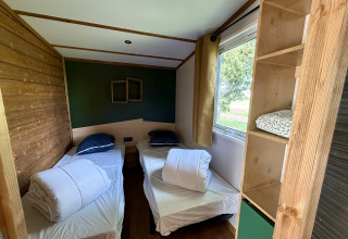 Værelse med to enkeltsenge, vindue med udsigt og reol i La Clairiere, Campsite Seasonova Ensoya, Frankrig.