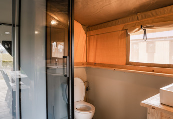 Salle de bain sous tente safari glamping avec toilettes, lavabo et fenĂŞtre au Holiday Park Eigen Wijze, Pays-Bas.