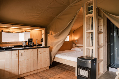 Interior de una tienda safari glamping con cocina, cama y calentador en Holiday park Eigen Wijze, Países Bajos.