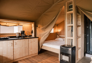 Intérieur d’une tente safari glamping avec kitchenette, lit et chauffage au Holiday park Eigen Wijze, Pays-Bas.