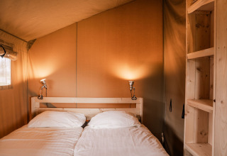 Habitación acogedora con cama doble y estanterías de madera en tienda glamping de Holiday park Eigen Wijze, Países Bajos.