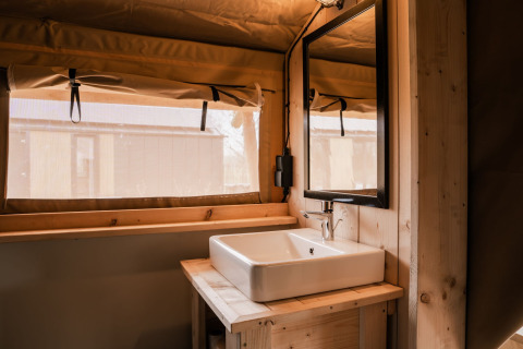 Interior de la tienda glamping tipo safari en Holiday park Eigen Wijze, Países Bajos, con lavabo y espejo.