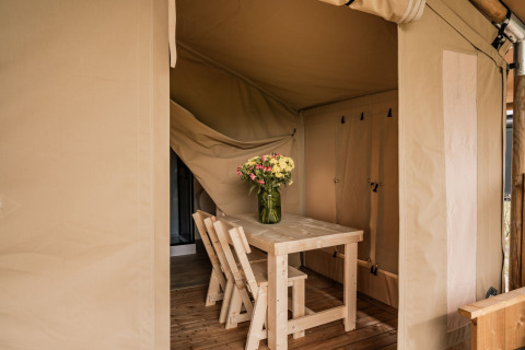 Vista interna di una tenda glamping con tavolo in legno, due sedie e vaso di fiori a Holiday park Eigen Wijze.