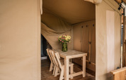 Indvendig udsigt over et glamping telt med et træbord, to stole og en vase med blomster på Holiday park Eigen Wijze.