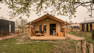 Geräumiges Safari-Glamping-Zelt mit einer Holzterrasse, Sitzgelegenheiten und grüner Umgebung.