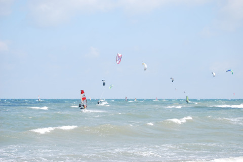 Windsurfers en kitesurfers genieten van de golven bij lodge Am Strand in Duitsland onder blauwe lucht.