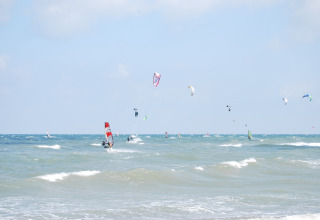 Windsurfers en kitesurfers genieten van de golven bij lodge Am Strand in Duitsland onder blauwe lucht.