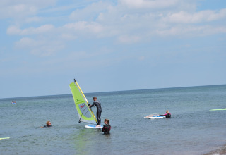 Verschillende mensen windsurfen bij de kust voor lodge «Am Strand» in Duitsland op een zonnige dag.