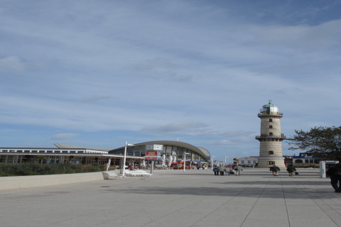 Uitzicht vanaf lodge Am Strand in Duitsland met vuurtoren, modern gebouw en mensen op het plein.