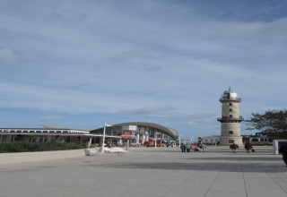 Uitzicht vanaf lodge Am Strand in Duitsland met vuurtoren, modern gebouw en mensen op het plein.