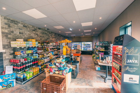 Supermarked i en lodge med drikkevarer, snacks, kaffe og køleskabe bagest på butikken, lyst interiør.