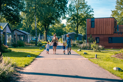 Family walking hand in hand down a path between modern lodges on a sunny day, surrounded by greenery.