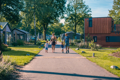 Family walking hand in hand down a path between modern lodges on a sunny day, surrounded by greenery.