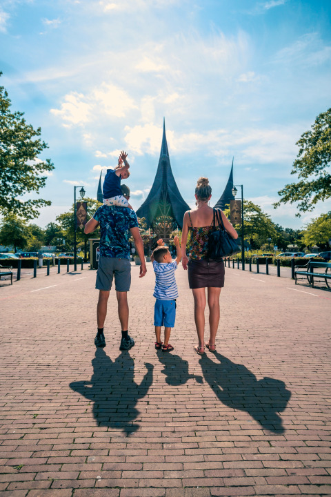 Family walking toward a fairy-tale style building on a sunny day, likely at the entrance of an amusement park.
