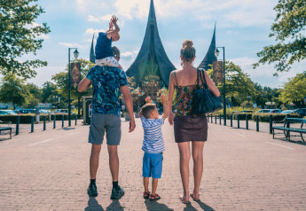 Gezin loopt op zonnige dag richting sprookjesachtig gebouw, vermoedelijk entree van een attractiepark.