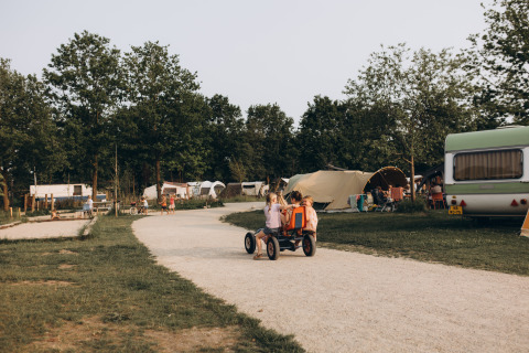 Kinder fahren auf einem Weg durch den Ferienpark De Kleine Wereld in Groningen, Niederlande, mit Zelten.