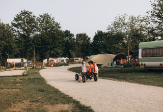 Kinder fahren auf einem Weg durch den Ferienpark De Kleine Wereld in Groningen, Niederlande, mit Zelten.
