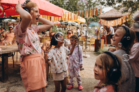 Kinder mit Kopfhörern spielen mit Seifenblasen auf dem Campingplatz De Kleine Wereld in Groningen, Niederlande.