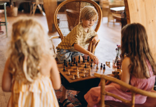 Kinder spielen gemeinsam Schach in einer gemütlichen Holzhütte im Ferienpark «De Kleine Wereld», Groningen.