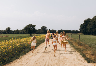 Kinder rennen einen Sandweg entlang an Blumenfeldern bei Onnen, Groningen, Niederlande, an einem sonnigen Tag.