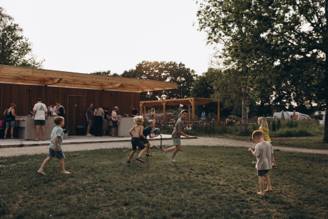 Niños juegan en el césped del camping De Kleine Wereld en Groningen, Países Bajos, mientras adultos conversan.