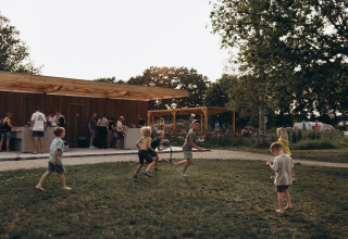 Niños juegan en el césped del camping De Kleine Wereld en Groningen, Países Bajos, mientras adultos conversan.