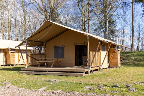 Tenda safari 6 con veranda in legno e tavolo da picnic, immersa nel verde e circondata da alberi.