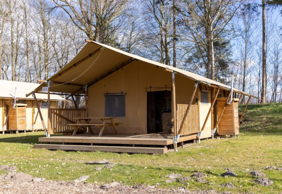 Safari tente 6 avec terrasse en bois et table, située dans un cadre naturel arboré et verdoyant.