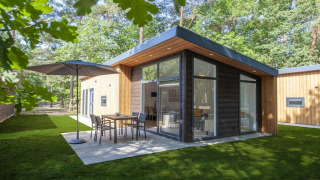 Tiny house Lodge Wellness 4 moderne avec grandes fenêtres, terrasse aménagée et cadre verdoyant.