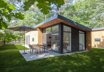 Modern Lodge Wellness 4 tiny house with large windows, patio furniture, and lush green surroundings.