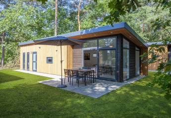 Tiny house Lodge 6 moderna con esterno in legno, ampie vetrate e patio immersa in una foresta verde.