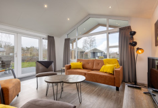 Moderne leefruimte in lodge Schipbeek 6 aan Tolplas, Nederland, met grote ramen en warme aankleding.
