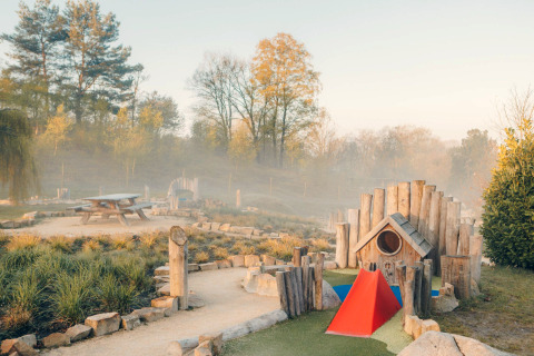 Speelplein en picknickbank bij een glamping accommodatie, omringd door natuur en bomen in ochtendmist.