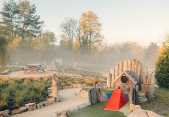 Legeplads og picnicbord omgivet af natur ved glamping indkvartering, med træer i baggrunden.