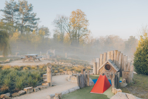 Playground and picnic table in a glamping accommodation, surrounded by nature and trees in morning mist.