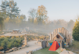 Playground and picnic table in a glamping accommodation, surrounded by nature and trees in morning mist.