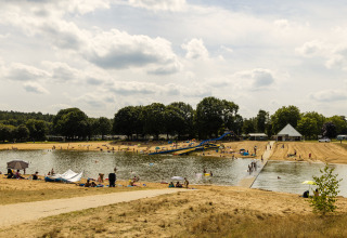 People enjoy a sunny day by a lake with a waterslide and sandy beach at a glamping accommodation.