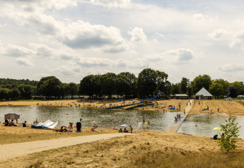 Des personnes profitent d’un lac avec toboggan aquatique et plage de sable dans un hébergement glamping.