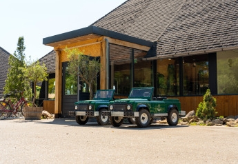Twee kleine groene speelgoedauto's Land Rover Defender geparkeerd voor de ingang van een glampingaccommodatie.