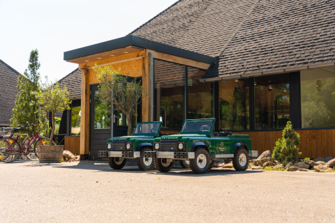 Two small green Land Rover Defender toy cars parked in front of a glamping accommodation entrance.
