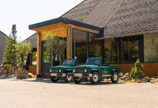 Two small green Land Rover Defender toy cars parked in front of a glamping accommodation entrance.