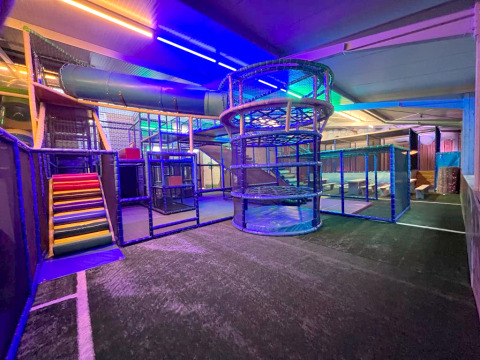 Indoor playground area with colorful slides and climbing structures, lit with LED lights at a glamping site.