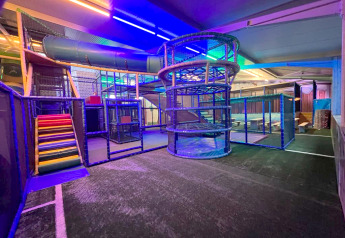 Aire de jeux intérieure avec toboggans et structures d’escalade, éclairée par LED, dans un glamping.