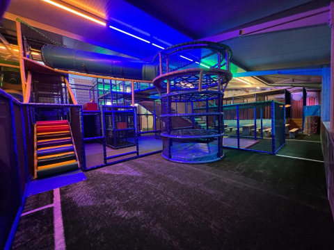 Indoor playground area with colorful slides and climbing structures, lit with LED lights at a glamping site.