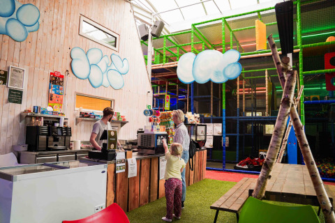 Indoor café and soft play area at a glamping site with a child and adult ordering at the counter.