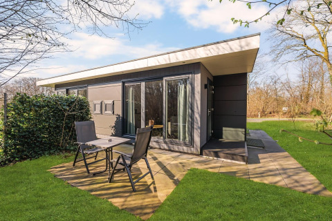 Modern nature house with patio, black outdoor chairs, and green lawn at Campsite Si-Es-An, Netherlands.