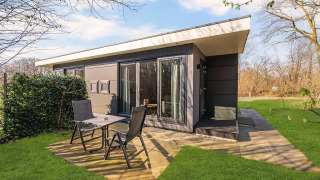 Moderne natuurhuis met terras, zwarte tuinmeubels en groene grasmat op Campsite Si-Es-An, Nederland.