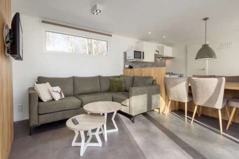 Sala en Chalet Comfort 6 de Hunzepark, Países Bajos, con sofá moderno, comedor y cocina integrada.
